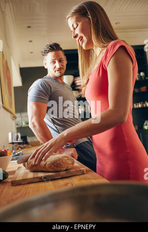 Aufnahme des jungen Paares stehen in Küche. Junge Frau schneiden Brot mit Mann durch. Frau, die Zubereitung des Frühstücks im Mittelpunkt. Stockfoto