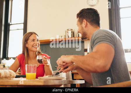Schuss der fröhliche junge Paar frühstücken in der Küche zu Hause. Junge Frau trinkt Kaffee mit Blick auf Mann lächelnd während sitt Stockfoto