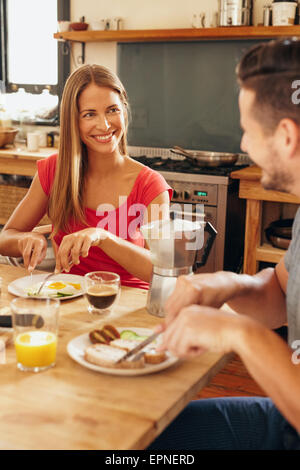 Glückliches junges Paar zu Hause frühstücken. Junge Frau und Mann sitzt am Frühstückstisch zusammen morgens frühstücken Stockfoto