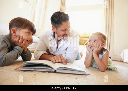 Innenaufnahme des jungen Mannes mit zwei Kindern ein Geschichte Buch. Familie mit einem Buch im Wohnzimmer auf dem Boden liegend. Stockfoto