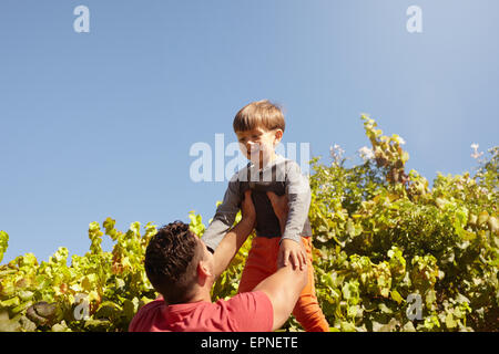 Schuss der Vater seinen Sohn hoch in die Luft heben. Glücklicher Vater und Sohn spielen im Freien an einem sonnigen Tag. Stockfoto