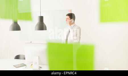 Geschäftsmann am Handy hinter Glaswand mit Klebstoff Noten sprechen. Konzeptbild der Unternehmensplanung. Stockfoto
