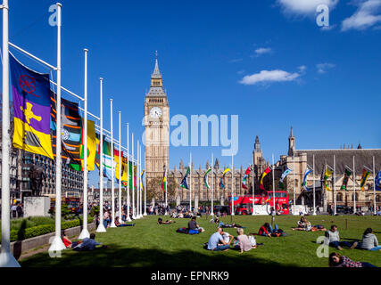 Touristen sitzen In der Sonne Bundesplatz vor den Houses of Parliament, London, England Stockfoto