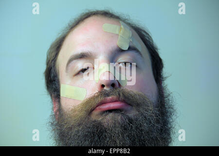 Ein trauriger bärtiger Mann hat Bandagen auf seinem Gesicht Stockfoto