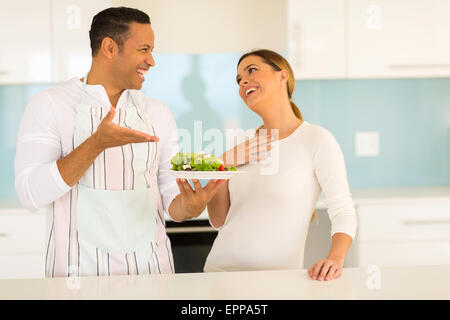 glücklicher Mensch grünen Salat zu seiner Frau in der Küche zu Hause geben Stockfoto