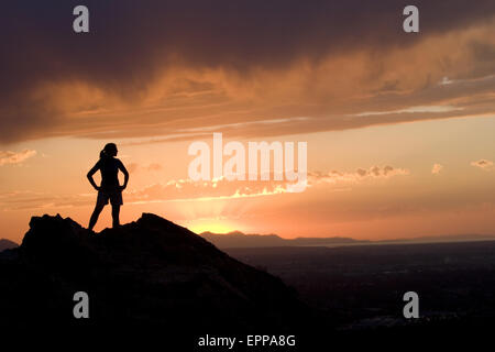 Frau in der Silhouette am Berg mit Blick auf eine Stadt Stockfoto