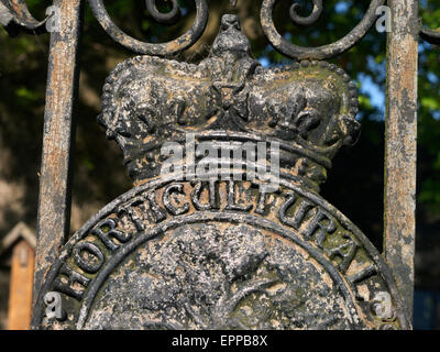 Close-up auf verwitterten Royal Horticultural Society (RHS) Metallplakette Emblem auf Eingangstore mit Gartenhäuschen hinter Stockfoto