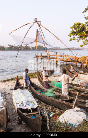 Lokale Fischer mit ihren Netzen und Angelboote/Fischerboote von einem traditionellen chinesischen Fischernetz an der Küste Fort Cochin, Kerala, Südindien Stockfoto