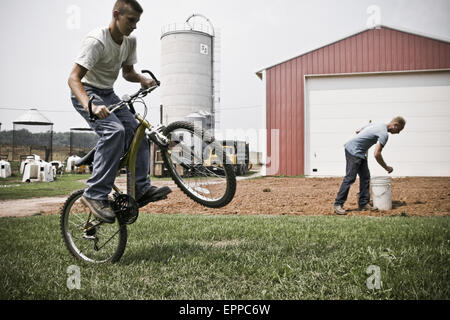 Ein Mann, die Vorbereitung des Bodens Pflanzenkulturen im Hinterhof des Bauernhauses, während ein Junge seine im Vordergrund Fahrradtouren. Stockfoto