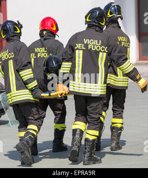 Vier tapfere Feuerwehrmänner tragen anderen Feuerwehrmann mit medizinischen Bahre Stockfoto