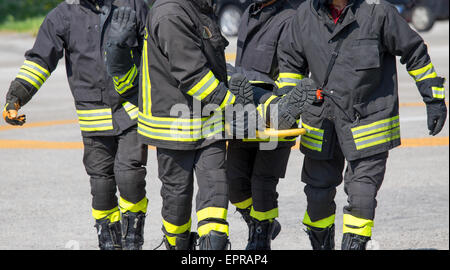 Vier tapfere Feuerwehrmänner tragen einen Feuerwehrmann mit medizinischen Bahre Stockfoto