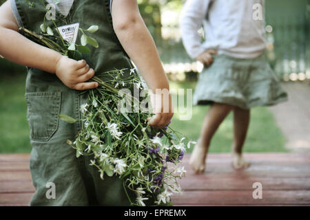 Ein Junge hält Blumen hinter seinem Rücken für ein Mädchen. Stockfoto