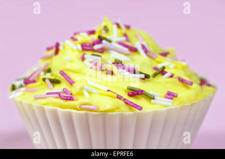 Ziemlich bunt dekorierten Kuchen oder Fee Kuchen mit gelber Zuckerguss und bunte Streusel auf einem rosa Hintergrund Stockfoto