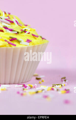 Ziemlich bunt dekorierten Kuchen oder Fee Kuchen mit gelber Zuckerguss und bunte Streusel auf einem rosa Hintergrund Stockfoto