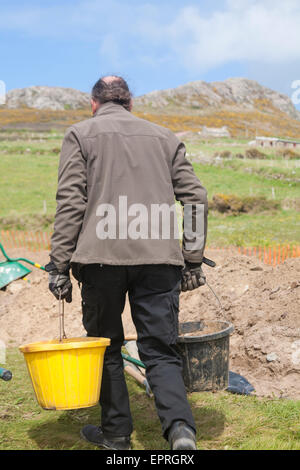 Mann bewegt und entleert Eimer für Aushubarbeiten in Whitesands Bay, Pembrokeshire Coast National Park, Wales, Großbritannien im Mai Stockfoto