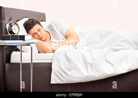 Junger Mann auf einem bequemen Bett schlafen bedeckt mit einer weißen Decke in einem Schlafzimmer Stockfoto
