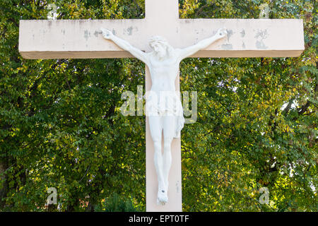 Das große hölzerne weiße Kreuz mit dem gekreuzigten Jesus Christus-Statue am Erscheinung Mountain in Medugorje unter grünen Bäumen und Unkraut Stockfoto