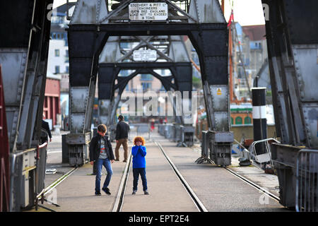 Zwei Jungs gehen unter die erhaltene Ladung Krane entlang der Hafenpromenade in Bristol. Stockfoto