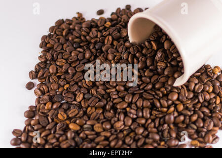 Nahaufnahme von vielen Kaffeebohnen aus einer Tasse auf weiß Stockfoto