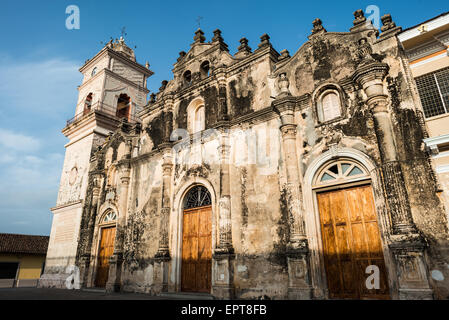 Barocke Fassade der Iglesia De La Merced Granada Nicaragua | GRANADA, Nicaragua — Geschwärzte Steinmetzarbeiten und freigelegter Putzzeichnen markieren die barocke Fassade der Iglesia de la Merced, deren kunstvolle Gesimse mit Zierknäufen neben dem angrenzenden Glockenturm aufragen. Die vernarbte Ostfront zeugt von der wiederholten Zerstörung der Kirche, einschließlich einer Brandstiftung durch die zurückziehenden Freischärlertruppen von William Walker im Jahr 1856, nach der der Turm bis 1862 wieder aufgebaut wurde. Stockfoto