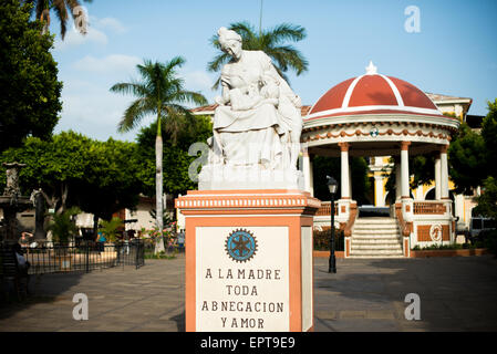 Mutterschaft Statue Parque Central Granada Nicaragua // GRANADA, Nicaragua — Eine Statue zu Ehren der Mutterschaft steht an prominenter Stelle im Parque Central, dem Hauptplatz und dem historischen Herzen von Granada. Auf dem Denkmal steht eine Inschrift mit der Aufschrift „Mutter aller Hingabe und Liebe“, die die Hingabe der Mutter feiert. Der Parque Central ist ein zentraler Treffpunkt für Einheimische und Besucher in Granada, einer der ältesten Kolonialstädte Nicaraguas. Der Platz ist von farbenfroher spanischer Kolonialarchitektur und wichtigen Bürgerhäusern umgeben. Dieses öffentliche Kunstwerk stellt eines von vielen Kulturdenkmälern dar Stockfoto