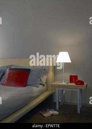 Schlafzimmer-Detail des Bettes mit einem kleinen Tisch, eine Lampe und ein Buch auf dem Boden Stockfoto
