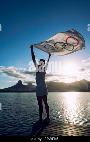 RIO DE JANEIRO, Brasilien - 5. März 2015: Athlet hält Olympische Flagge über dem Sonnenuntergang City Skyline Blick in Lagoa Rodrigo de Freitas. Stockfoto