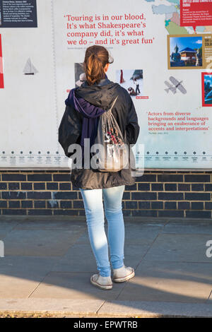 Junge Frau liest Plakate an Shakespeares Globe Theatre, Bankside, London im Mai Stockfoto