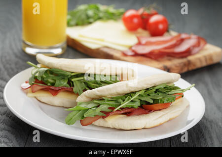 zwei Sandwiches mit Schinken, Rucola und Tomaten im Fladenbrot auf Platte, auf Holztisch Stockfoto