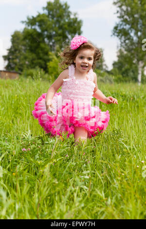 fröhliches Mädchen im rosa Kleid läuft auf einer Wiese Stockfoto