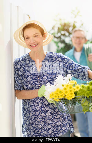 Lächelnde senior Frau mit Blumen mit senior Mann im Hintergrund Stockfoto