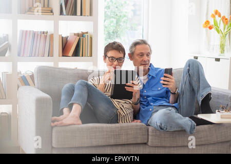 Älteres Paar Austausch von elektronischen Geräten auf sofa Stockfoto