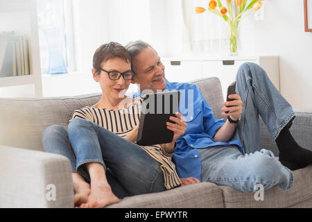 Älteres Paar Austausch von elektronischen Geräten auf sofa Stockfoto