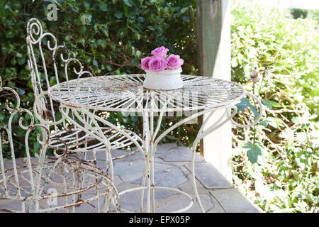Weißen Schmiedeeisen Gartentisch und Stühle auf der Terrasse mit Vase mit rosa Rosen in südafrikanischen Heimat