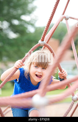 Junges Mädchen spielt an einem Seil klettern Struktur auf eine Outdoor-Park Spielplatz Stockfoto