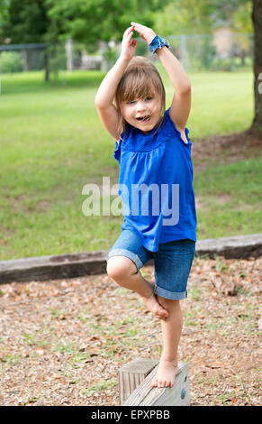 Kind zu Fuß auf einer Outdoor-Holz Schwebebalken mit einer Ballerina pose Stockfoto