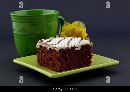 Reichlich leckere roter Samt-Kuchen auf zeitgenössische grün, quadratische Platte mit klassischen Becher und gelbe Blume hinter. Stockfoto