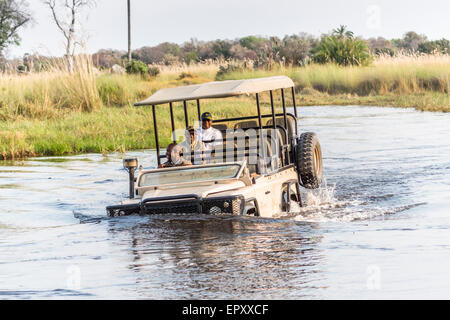 Safari-Jeep mit Fahrer und Touristen Lachen und Spaß, fording einen tiefen Fluss in das Okavango Delta, Botswana Stockfoto