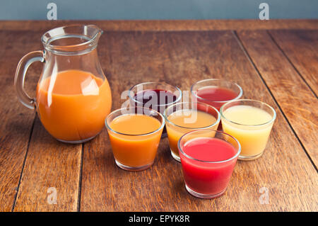 Krug und sechs Gläser verschiedenster Säfte auf einem Holztisch Stockfoto