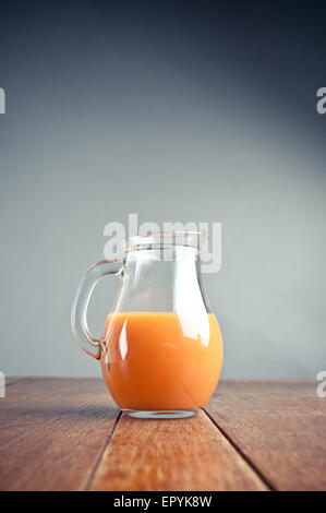 Krug mit Karotte und Orangensaft auf einem Holztisch mit einfachen bläulichen Hintergrund Stockfoto