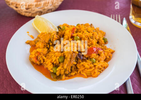 Teller mit leckeren gelben Safran bunt gemischte Paella auf einem weißen Teller mit einer Scheibe Zitrone serviert. Stockfoto