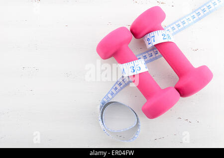 Gesundheit und Fitness-Konzept mit rosa Hanteln und Maßband auf weiße distressed Holztisch Hintergrund. Stockfoto