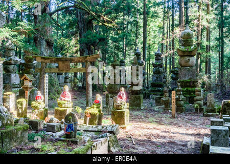 Der berühmte Friedhof von Okunoin in Koyasan in Japan. Sonnendurchflutete Waldlichtung, mit vier Jizo-Statuen, Steintorii und Reihe von Gorinto fünf Steinpagoden. Stockfoto