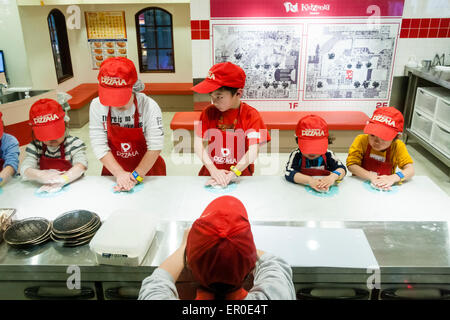 Kinderaktivitätszentrum Kidzania in Nishinomiya, Japan. Blick über den Leiter des Lehrers einer Linie von fünf Kindern Rollen Teig zu Pizzen zu machen. Stockfoto