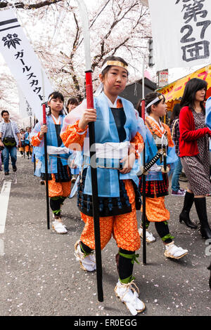 Ein Team von Kindern, Mädchen, die als Shimobe-Soldaten der Heian-Ära verkleidet in der Frühlingsparade unter Kirschblüten in Tada, Japan marschieren. Stockfoto