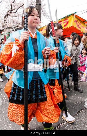 Ein Team von Kindern, Mädchen, die als Shimobe-Soldaten der Heian-Ära verkleidet in der Frühlingsparade unter Kirschblüten in Tada, Japan marschieren. Stockfoto