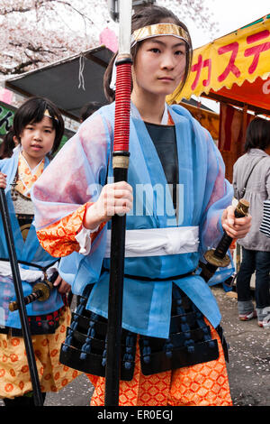 Ein Team von Kindern, Mädchen, die als Shimobe-Soldaten der Heian-Ära verkleidet in der Frühlingsparade unter Kirschblüten in Tada, Japan marschieren. Stockfoto