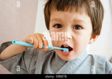 Nahaufnahme von kleinen Kind, Junge, Zähneputzen mit Kinderzahnbürste beim Betrachten des Betrachters. Drinnen. Kopf- und Schulteransicht. Tageslicht. Stockfoto