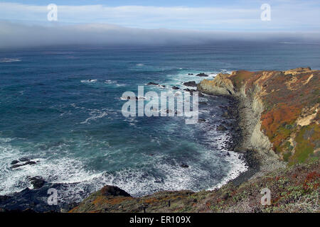 Eine graue Nebelbank rollt auf den blauen Pazifik entlang der zerklüfteten Küste am Big Sur in Zentral-Kalifornien, USA. Stockfoto