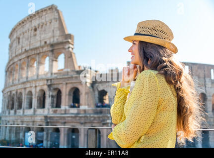 Eine Frau Tourist ist stehend, stützte sich ihr Kinn auf ihre Hände und Blick in die Ferne und lächelnd. Sie ist die Aussicht bewundern. In der Ferne, das Kolosseum an einem heißen Sommertag. Stockfoto